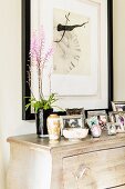 Detail of framed family photos arranged on chest of drawers below drawing on wall