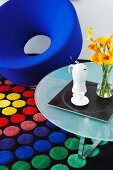 Bright blue, hoop-shaped chair and side table on rug with pattern of colourful circles