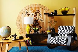 Armchair with black and white upholstery and retro table in front of unusual shelving with painted wooden back wall