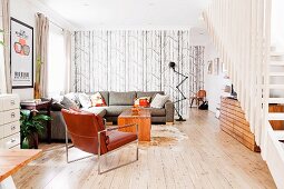 Spacious interior with leather armchair and grey corner couch in open-plan lounge area behind staircase