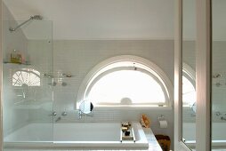 Bath and shower with glass screen in front of semi-circular window in bathroom