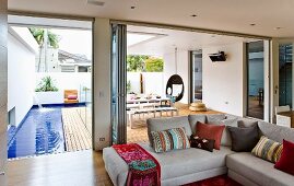 Living room with corner sofa & open folding doors leading to deck-style terrace with pool