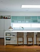 weiße Einbauküche mit modernen Fronten, ein Vintage Wandschrank und Korbstühlen an der Küchentheke