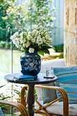 Bouquet of white flowers in blue china vase on round side table in front of glass balustrade