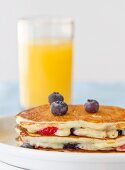 Buttermilch-Pancakes mit Blaubeeren und Erdbeeren und ein Glas Orangensaft