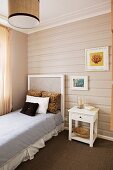 Horizontal wood cladding on wall behind single bed and white, nostalgic bedside table
