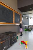 Offener Wohnraum mit alter Wandtafel in umgenutztem Schulhaus; alte Transportkisten und buntes Holzrad auf poliertem Betonboden