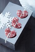 Wrapped Christmas present decorated with red and white checked fabric hearts and wooden snowflake