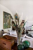 Bouquet of grasses and peacock feathers on retro cabinet; sofa and chair in background
