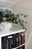 Dried flower arrangement in ceramic vessel on simple, white bookcase