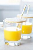 Glasses of orange juice with biscuit lids and drinking straws