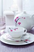 A place setting for afternoon tea and a teapot, all decorated with a flower motif