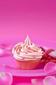 A pink strawberry cupcake with raspberries and rose petals