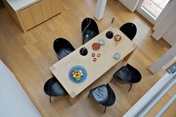 View down onto modern dining table with black shell chairs on wooden floor