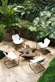 Cantilever chairs with canvas seats and original tree trunk table on pale stone flagged floor surrounded by tropical garden vegetation