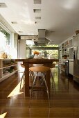 Large window and glass wall in white, modern kitchen with 80s bar stools at natural wooden counter