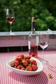 A bowl of strawberries and some rosé wine on a table on the balcony, the table covered with a gingham tablecloth