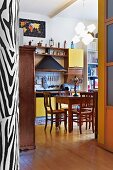 Blick in Küche auf rustikalem Essplatz vor Küchenzeile und Dunstabzug neben Hängeschränken mit gelber Front