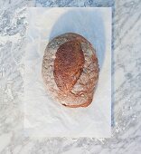 A loaf of bread on a piece of paper, on top of a marble surface dusted with flour