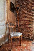 Gepolsterter Stuhl mit vergoldetem Holzrahmen im Rokokostil und Prozessionsstab an Ziegelwand in Zimmerecke