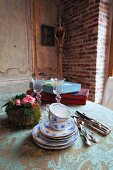 Stack of blue and white painted teacups and saucers next to silver cutlery and flower arrangement on vintage tablecloth in corner of rustic dining room