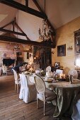Enthusiasts' collection of antiques in salon of French country manor with romantic dinner table below rustic exposed roof structure