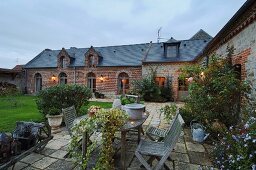 Gemütlicher Gartenhof eines französischen Landgutes mit Holztisch und Klappstühlen auf alten Steinplatten