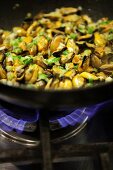 Mussels and spring onions being sautéed in a frying pan