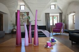 Vases in various shades of purple on table and black leather sofa in spacious living room with vaulted ceiling