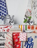 Colourful tea towels hanging on wall and lying on table