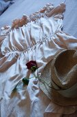 Rose and straw hat arranged on dress spread out on bed