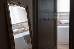 Gilt-framed mirror next to open interior door with view into bathroom