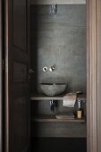 Blick durch offene Tür auf schlichte Waschschüssel auf Holzplatte an Wand in Spachteltechnik-Optik