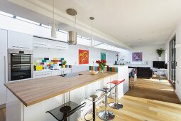 Kitchen counter with pale wood worksurface and bar stools in open-plan interior