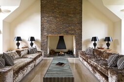 Theatrical seating area with lustrous velvet sofas and dominant table lamps against stone-clad chimney breast
