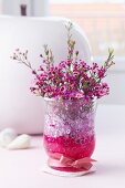 Posy of waxflowers (Chamelaucium uncinatum) in glass vase with decorative pebbles