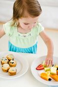 Girl (2-3) choosing between fruit salad and muffins