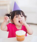 Portrait of baby girl (12-17 months) in party hat eating cupcake