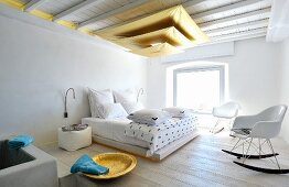 Pendant lamp made from three suspended gold sails in Mediterranean bedroom with Bauhaus rocking chair in front of double bed