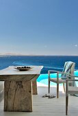 Rustikaler Tisch und Stühle mit weißem Geflecht auf Terrasse vor Pool und Blick auf das Meer
