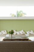 Rückseite einer Couch vor Tisch und Sitzbank mit Kissen an grün getönter Wand mit Oberlicht