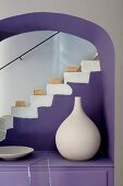 weiße Tonvase auf lila Kommode in Rundbogen Nische vor Treppenaufgang künstlerisch arrangiert