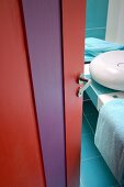 Blick durch offene, rot und lila lackierte Badtür auf modernes Waschbecken auf gefliester Platte