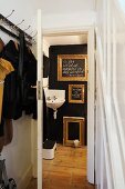 Coat rack in foyer and view of gilt picture frames on black wall and corner sink through open door