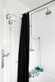 Vintage hooks on door and open, black shower curtain in front of bathtub with shower head on wall