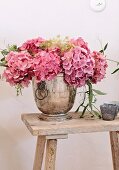Pink hydrangea flowers in silver vessel on rustic wooden stool