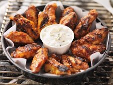 Barbecued chicken wings with dip in a tray on the barbecue