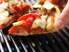 A hand reaching for a slice of pizza on the barbecue