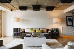 Loftartiger Wohnraum mit kubischem Couchtisch vor eleganter Sofagarnitur zwischen Designer Leuchten