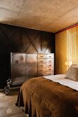 Blick über Bett auf Vintage Metallschrank mit Rollen vor Holzpaneelwand und Kettenvorhang in Schlafzimmer